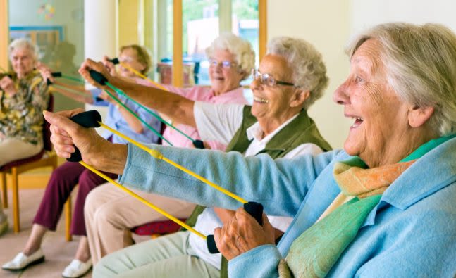 Five older women use exercise bands while sitting in chairs